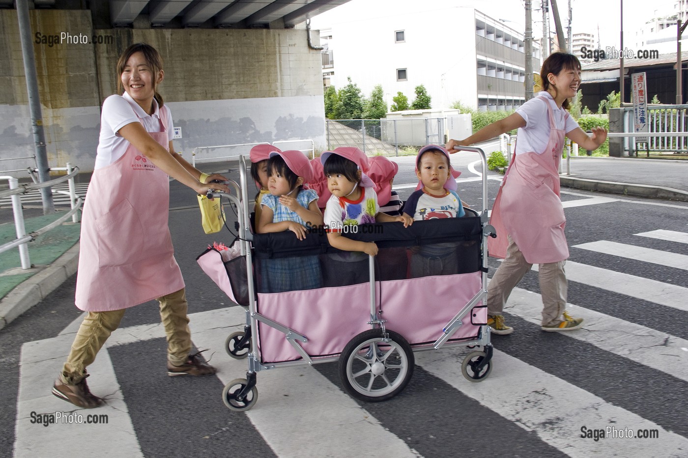 ENFANTS DANS UNE POUSSETTE COLLECTIVE TIREE PAR DES PUERICULTRICES JAPONAISES SUR UN PASSAGE PIETON, TOKYO, JAPON 