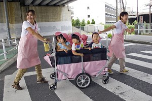 ENFANTS DANS UNE POUSSETTE COLLECTIVE TIREE PAR DES PUERICULTRICES JAPONAISES SUR UN PASSAGE PIETON, TOKYO, JAPON 